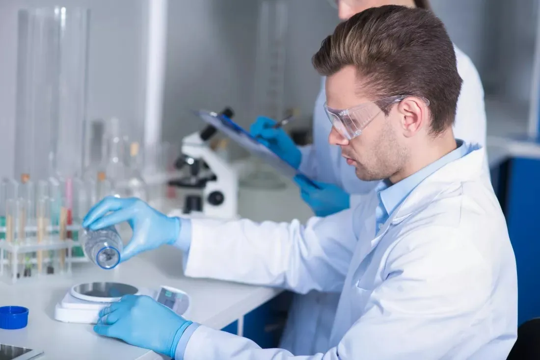 Jeune chercheur portant des lunettes de protection pese des substances sur une balance de laboratoire
