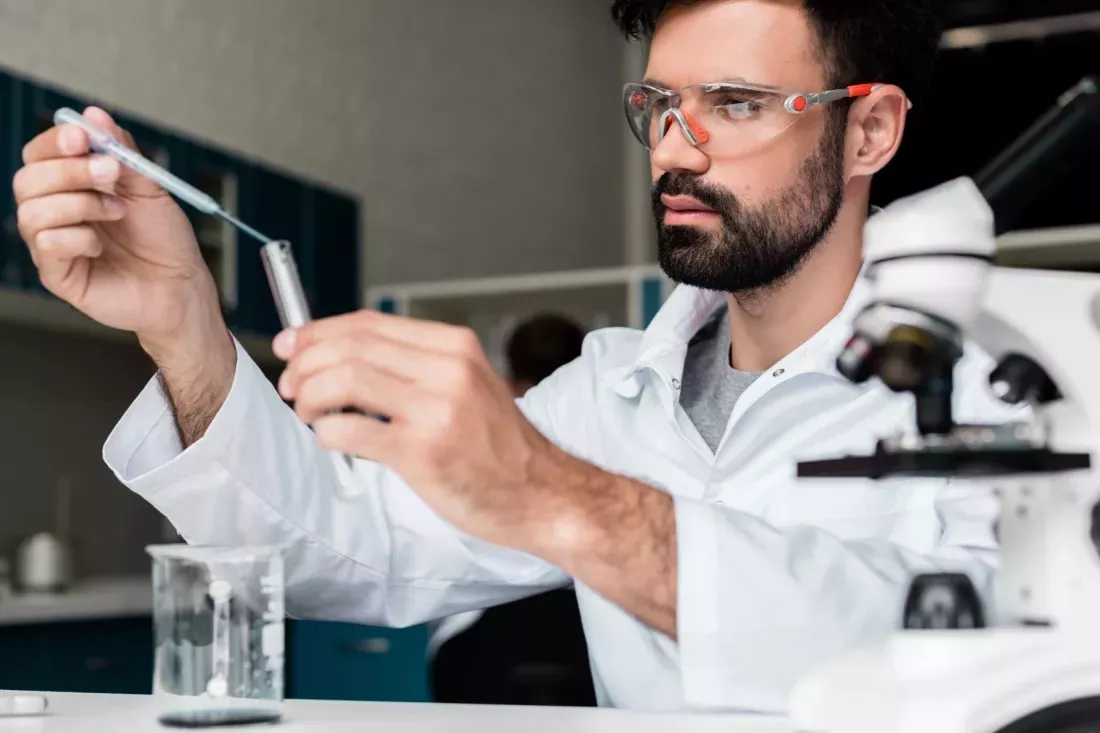 Scientifique avec des lunettes de protection versant a la pipette un echantillon dans un tube a essai dans un laboratoire de chimie