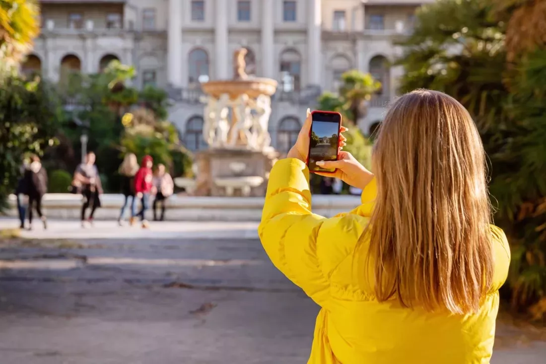 Jeune femme en veste jaune photographiant une place avec son telephone